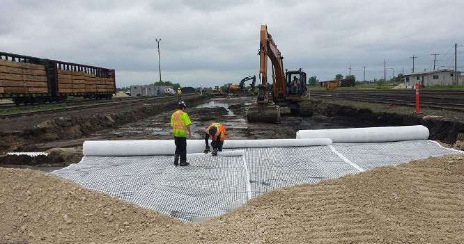 Workers laying geosynthetics on road rehabilitation project